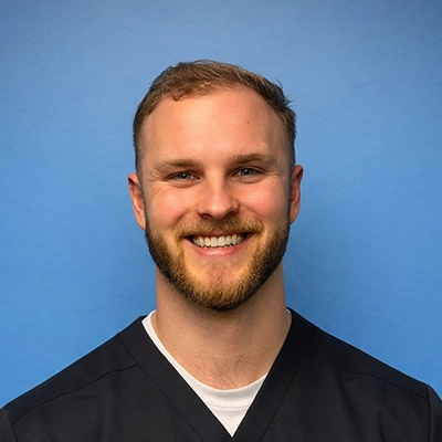 Chiropractor Joseph (Jet) Trout Smiling In Front Of Blue Background