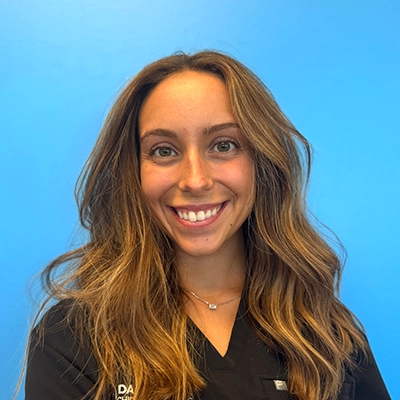 Receptionist And Chiropractic Assistant Carly Smiling In Front Of Blue Background